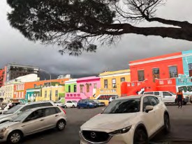 Cars parked outside of the city, with colorful buildings in the background.