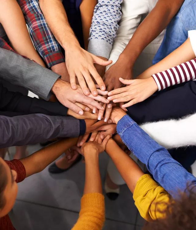 Close up of about a dozen people in a circle, putting hands together in the center