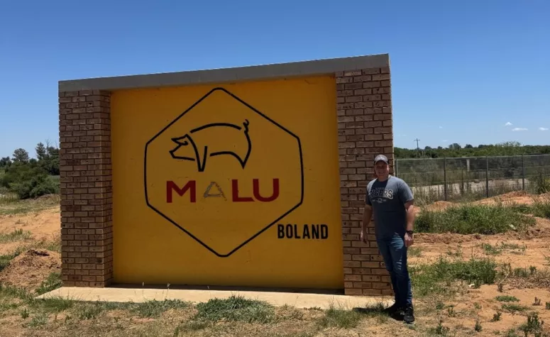Dr. Johnson stands by a large sign for the Malu pork production site