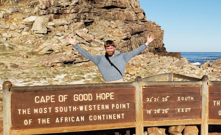 Student G. Behrends standing behind a wooden sign for the Cape of Good Hope