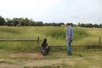 Two people look at a large grassy field behind a low wooden fence