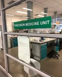 "Precision Medicine Unit" sign on the glass entrance to a lab