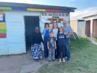 A small group of people pose outside a small white building.