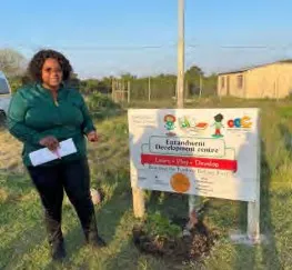 A woman stands by a sign for a project