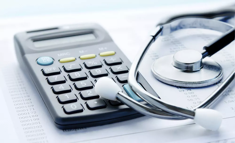 Calculator on top of scattered papers with out-of-focus medical code information; sethoscope set to side, briefly overlapping calculator at bottom right corner