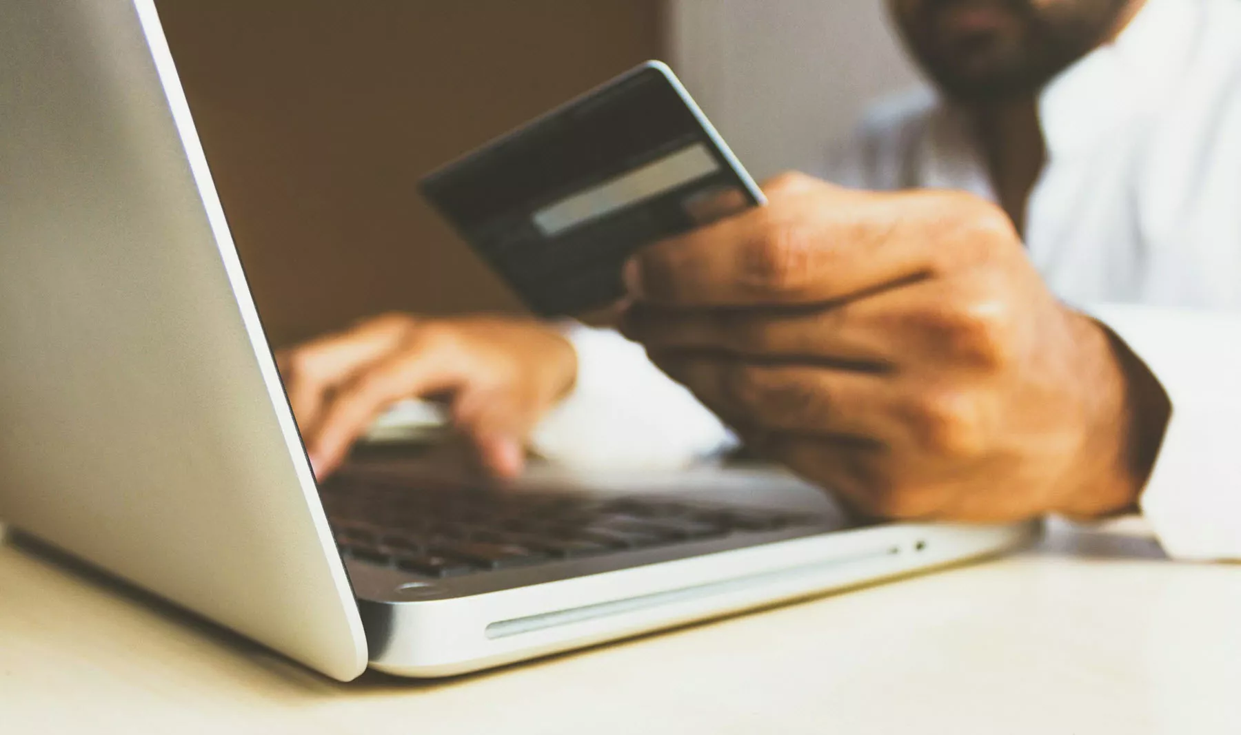 Close up of man's hands with laptop; right hand is placed on keyboard; left hand holds a payment card