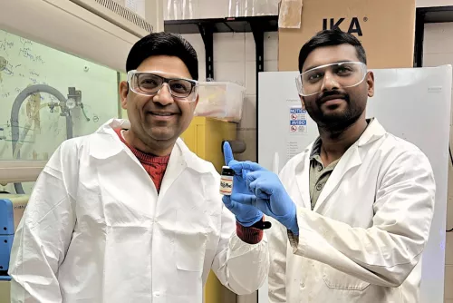 Two researchers in lab coats and protective goggles holding a container