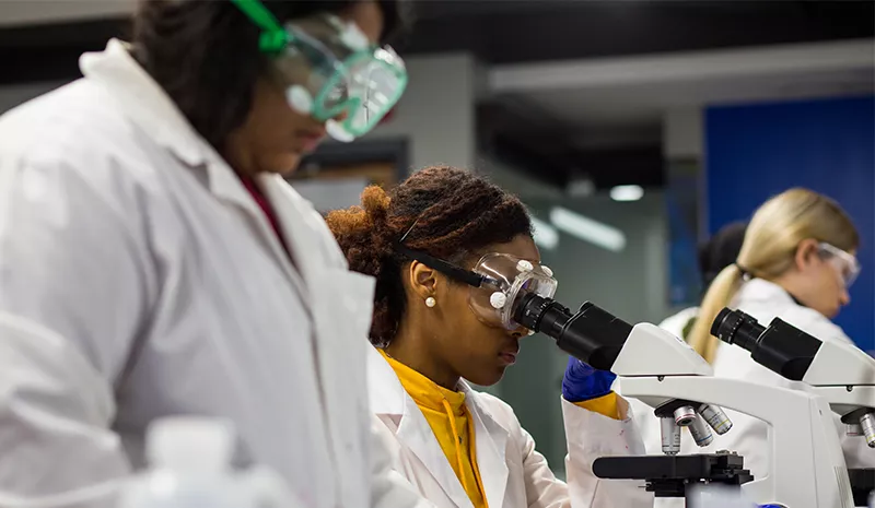 student in white lab coats looking through microscope
