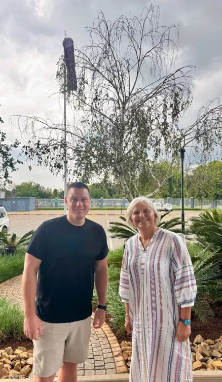 Dr. Johnson and Dr. van Marle-Koester pose in front of green plants at the edge of a parking lot