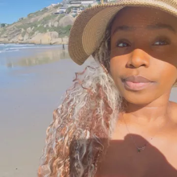 Selfie of student Denise Brown wearing a woven hat at the beach in Cape Town